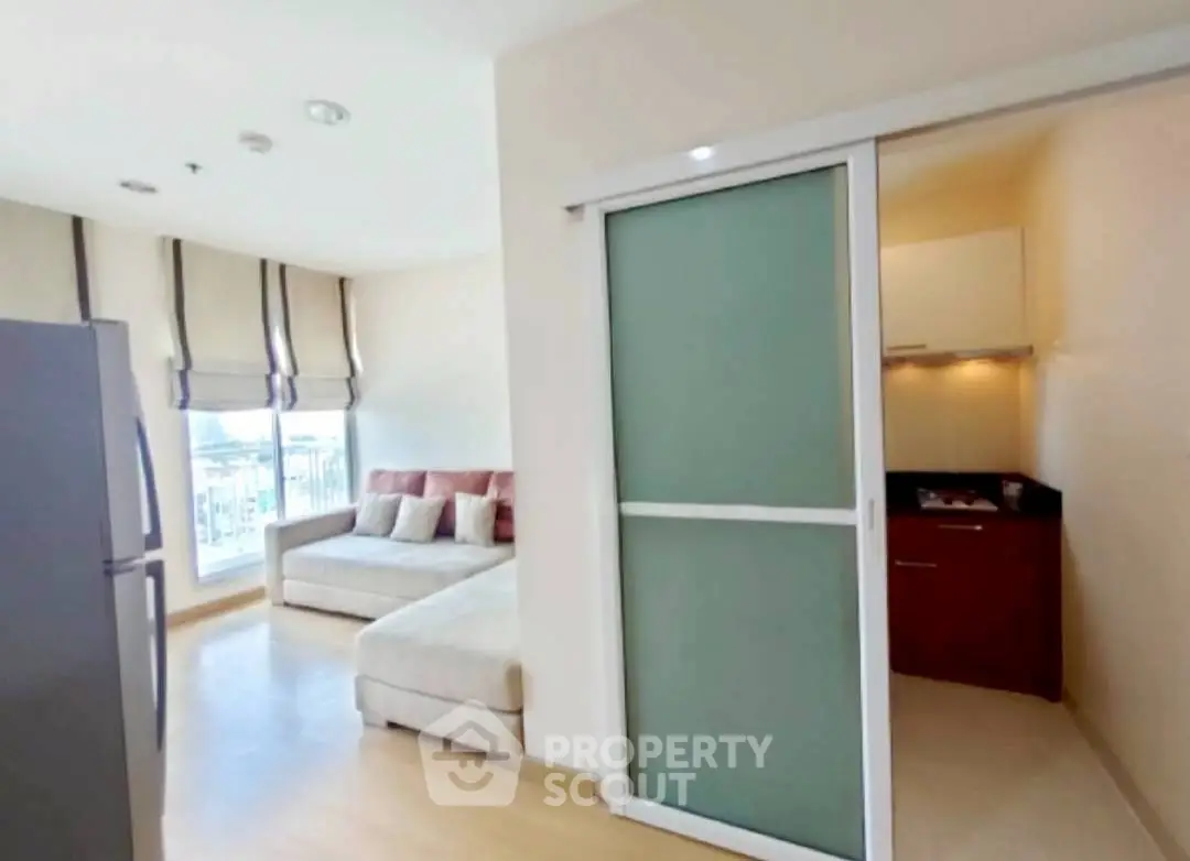 Modern living room with sliding door to compact kitchen, featuring a cozy sofa and natural light.