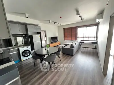 Modern open-plan living room with kitchen, featuring sleek furniture and natural light.