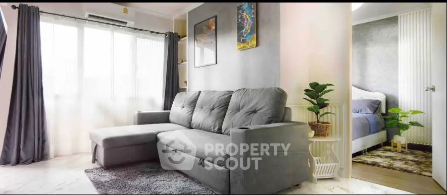 Modern living room with gray sofa and natural light, adjacent to a cozy bedroom.