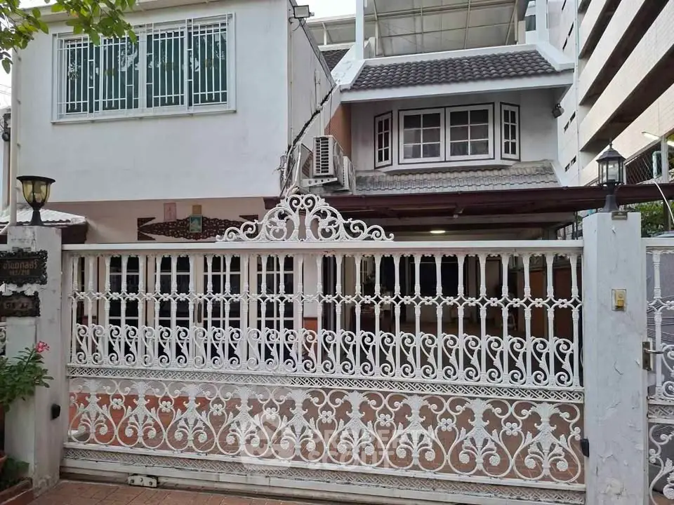 Charming two-story house with ornate white gate and lush greenery, perfect for family living.