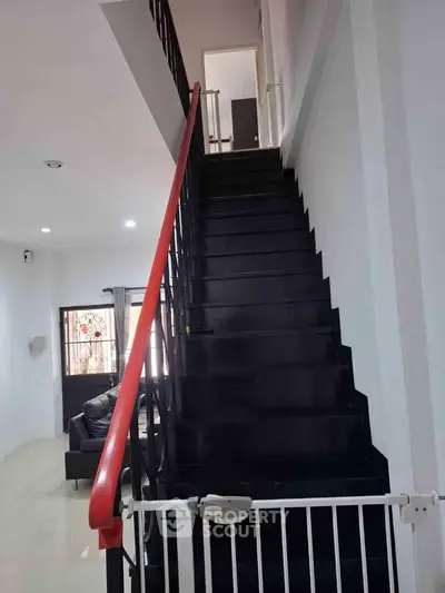 Modern staircase with sleek black steps and red handrail in a contemporary home interior.