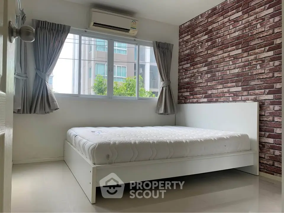 Modern bedroom with brick accent wall and large window in urban apartment
