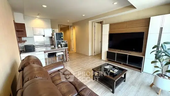 Spacious modern living room with leather sofa and large TV, open to sleek kitchen area.