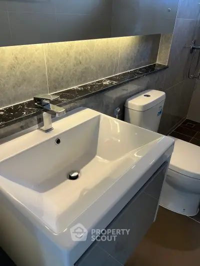 Modern bathroom with sleek sink and toilet, featuring elegant tile design and ambient lighting.