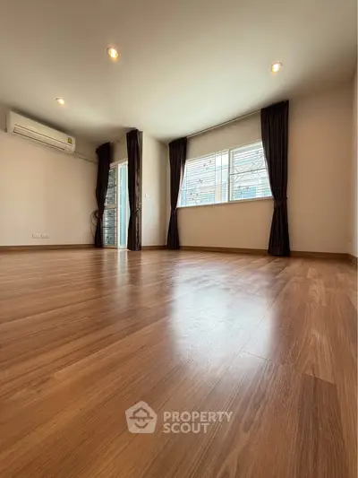 Spacious empty room with wooden flooring and large windows, ideal for customization.