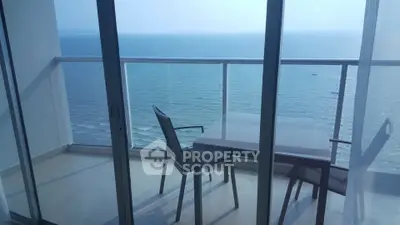Stunning ocean view from modern balcony with glass railing and outdoor seating.