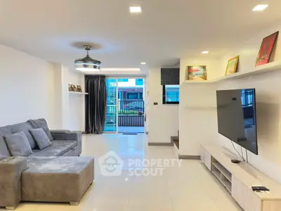Spacious modern living room with large TV and cozy gray sofa, featuring elegant decor and ample natural light.