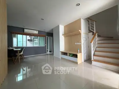 Spacious modern living area with dining space and staircase, featuring sleek design and ample natural light.