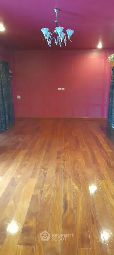 Spacious room with polished wooden floors and elegant chandelier lighting.