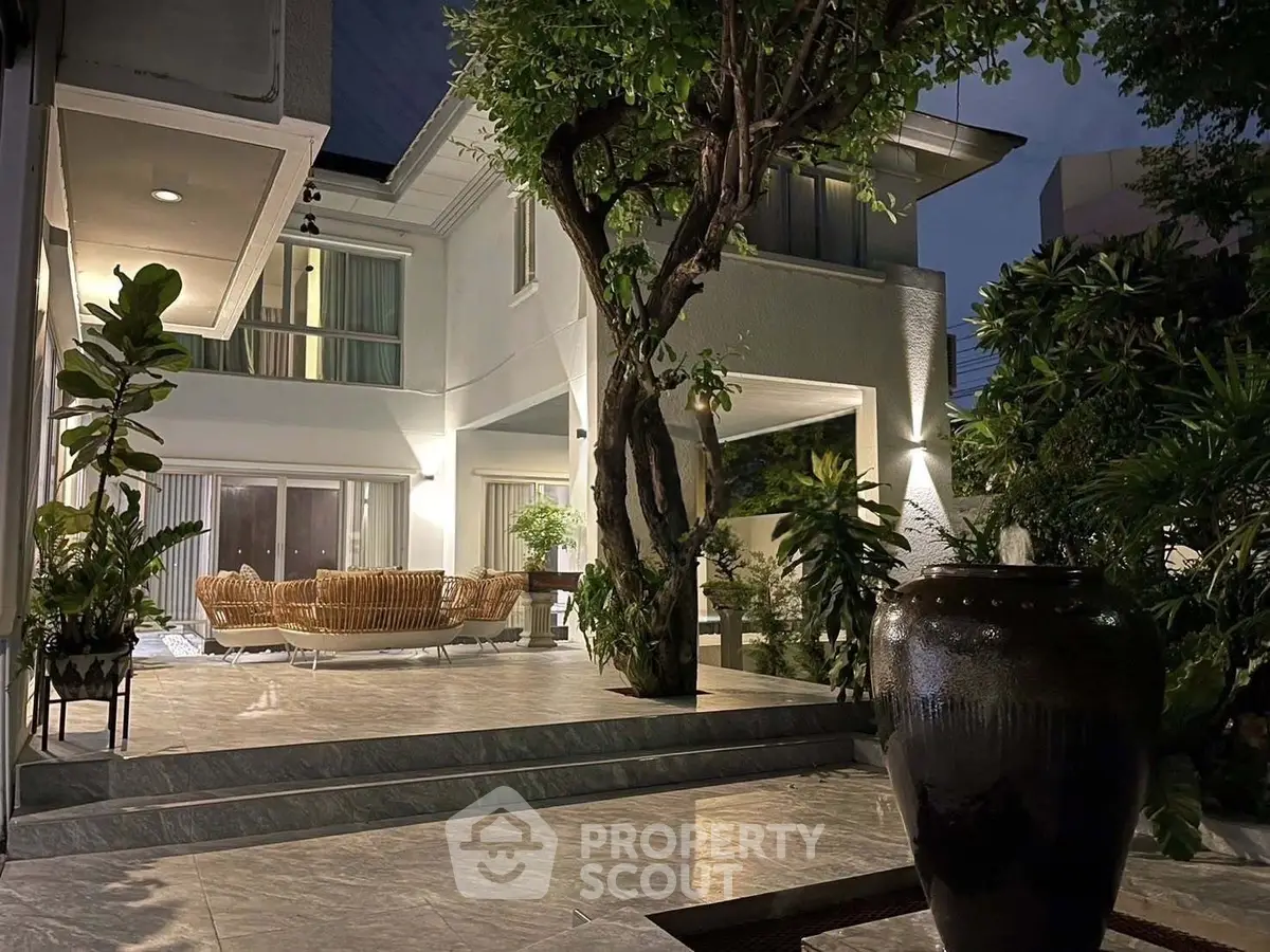 Luxurious modern home exterior with elegant patio and lush greenery, perfect for evening relaxation.