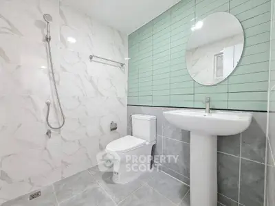 Modern bathroom with sleek design, featuring a round mirror, pedestal sink, and elegant shower area.