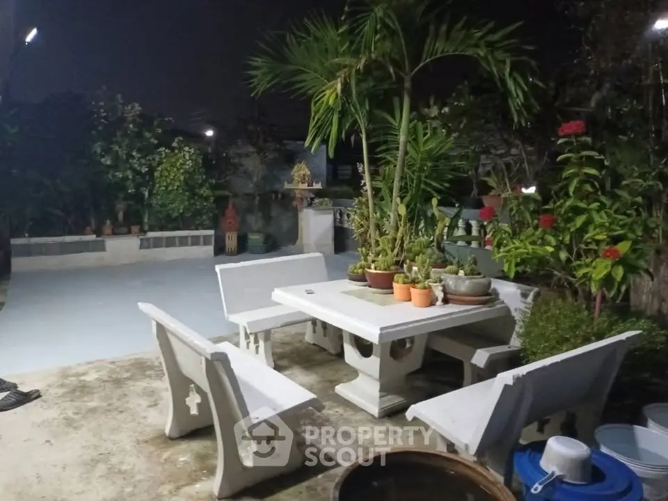 Charming garden patio with white stone furniture and lush greenery, perfect for outdoor relaxation.
