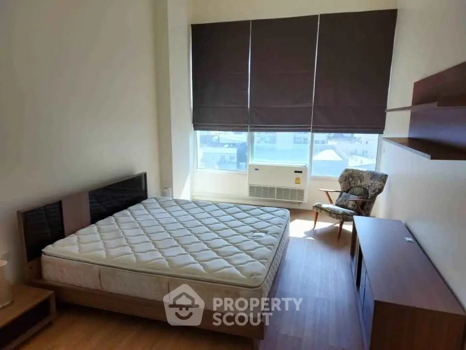 Spacious bedroom with large window and modern furnishings, perfect for urban living.