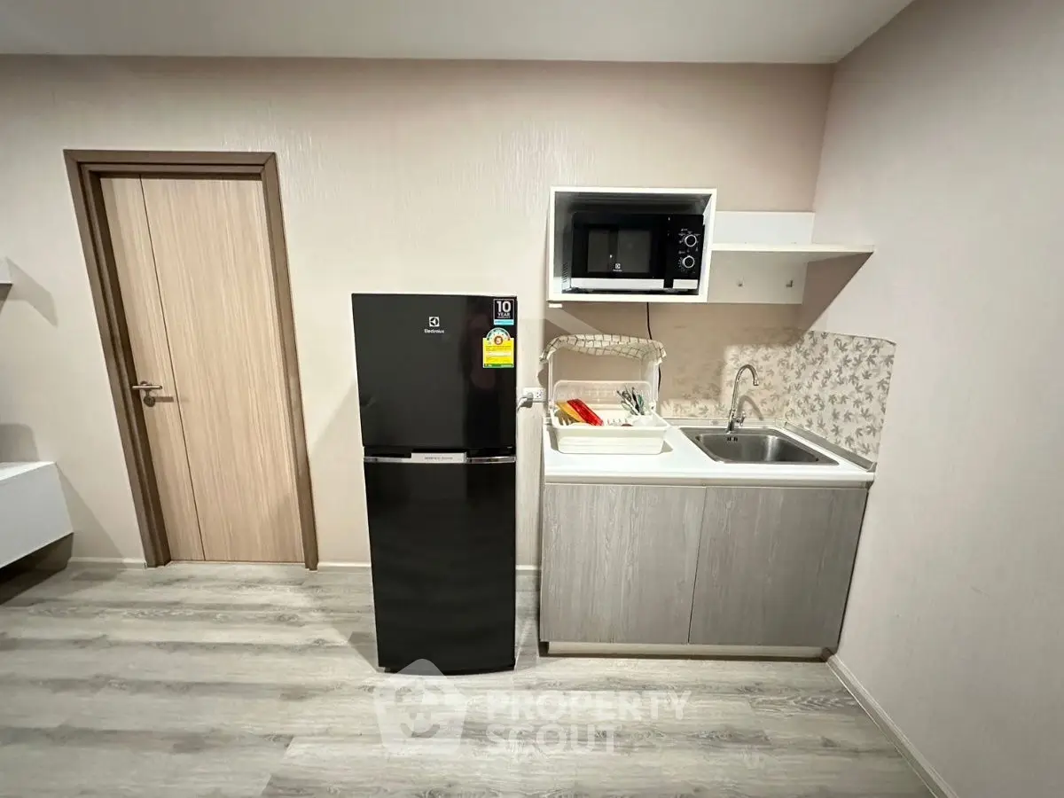 Modern kitchen with sleek appliances and minimalist design, featuring a black fridge and microwave.