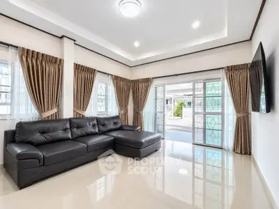 Spacious living room with modern black leather sofa and large windows for natural light.