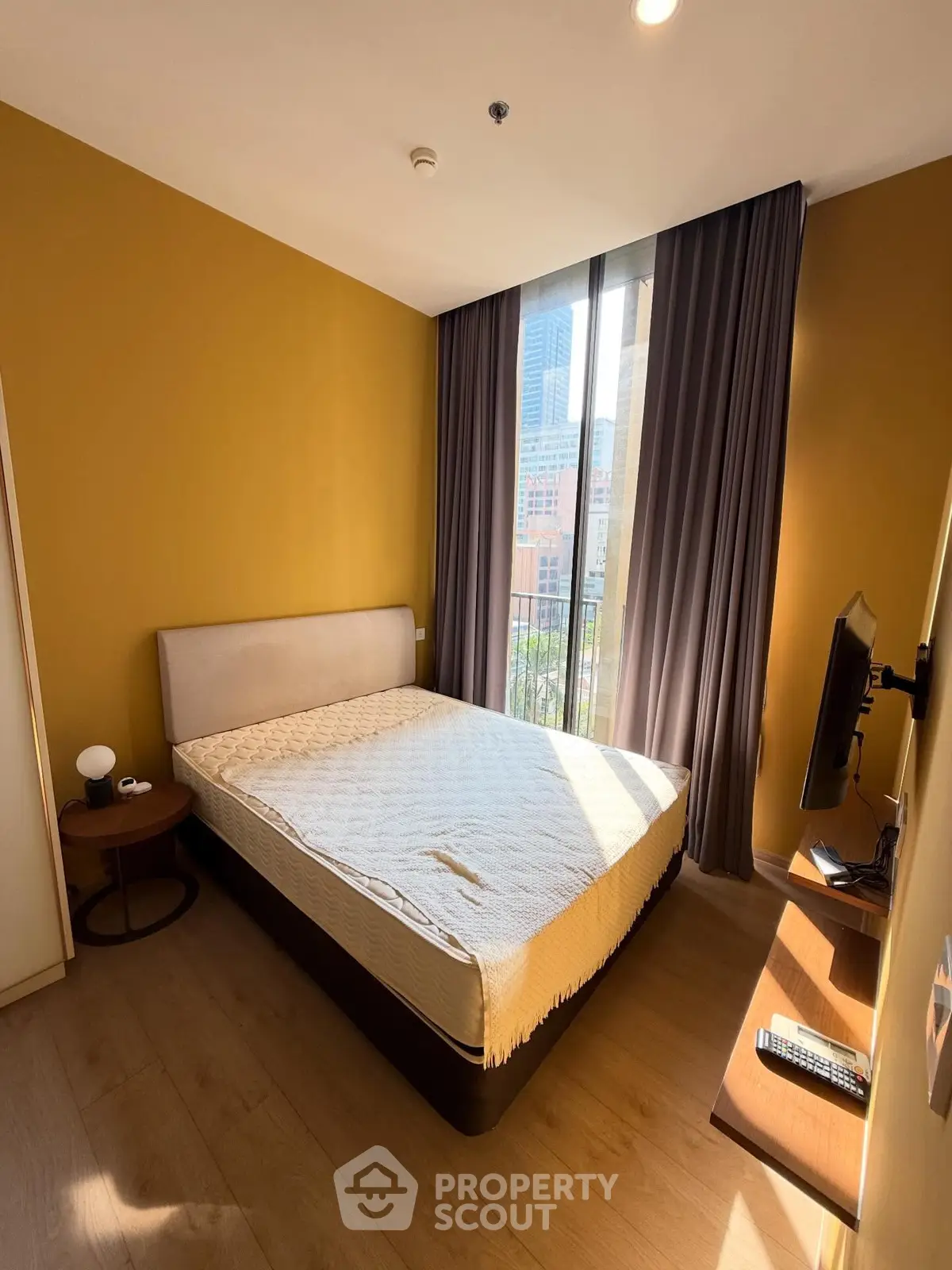 Cozy bedroom with large window and city view, featuring modern decor and natural light.