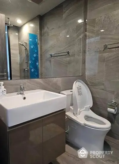 Modern bathroom with sleek marble tiles and glass shower enclosure, featuring a stylish sink and toilet, perfect for contemporary living.