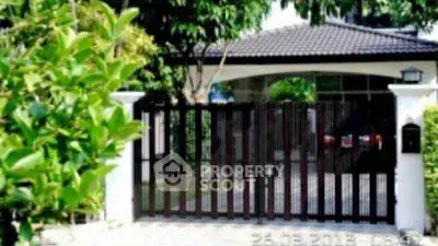 Charming gated entrance of a modern home with lush greenery and sleek design.