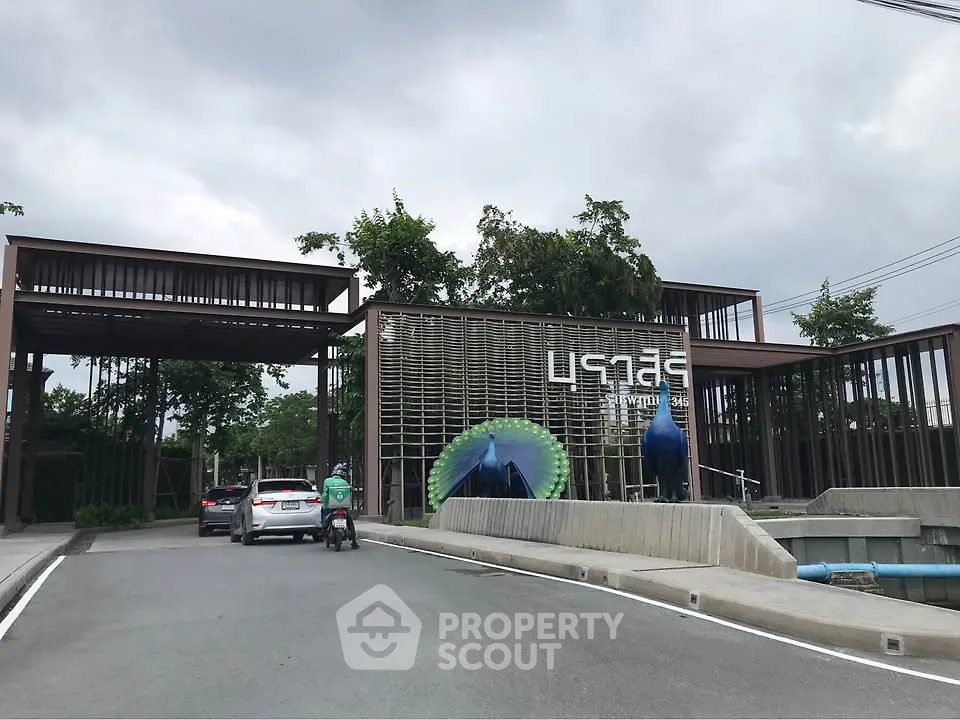 Modern gated entrance with unique architectural design and lush greenery.