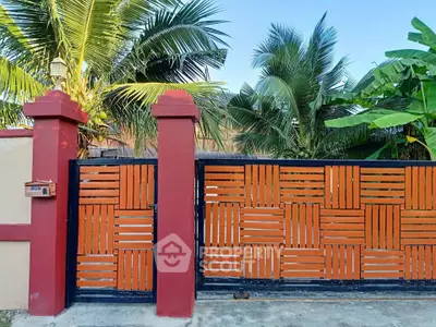 Charming tropical home entrance with wooden gate and lush palm trees.