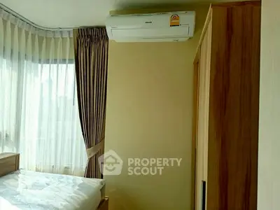 Bright bedroom with large window and air conditioning unit, featuring modern curtains and wooden furniture.
