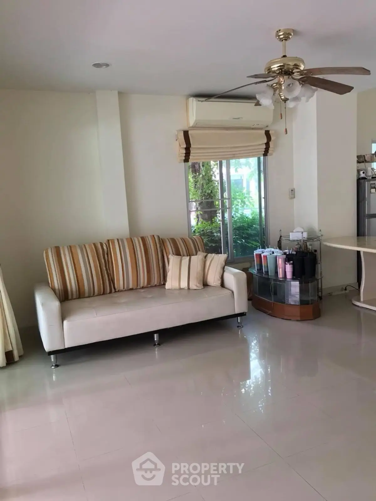 Spacious living room with modern sofa and ceiling fan, featuring large windows for natural light.