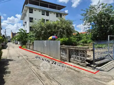 Spacious land plot with gated entrance and adjacent building, ideal for development.