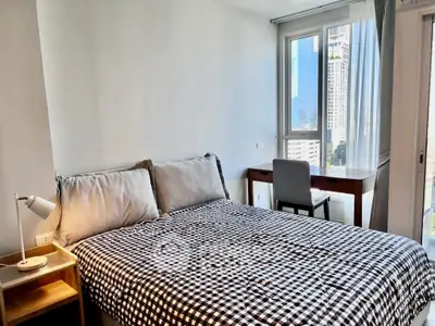 Modern bedroom with city view, featuring cozy bed and stylish desk setup.