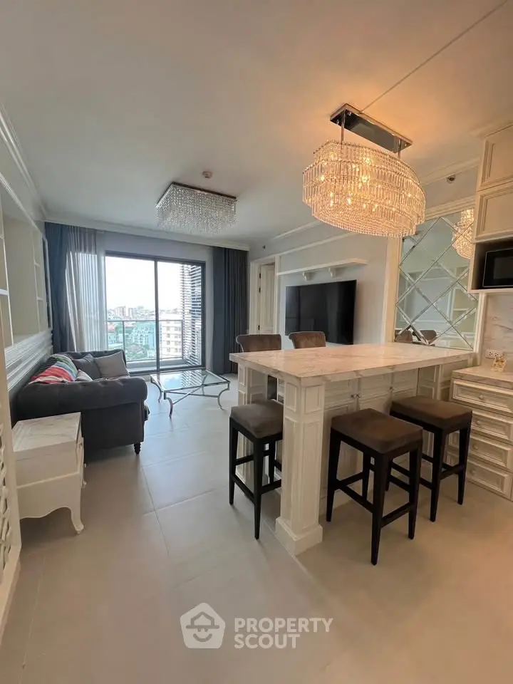 Luxurious living room with elegant chandelier and city view, featuring modern open kitchen and stylish decor.