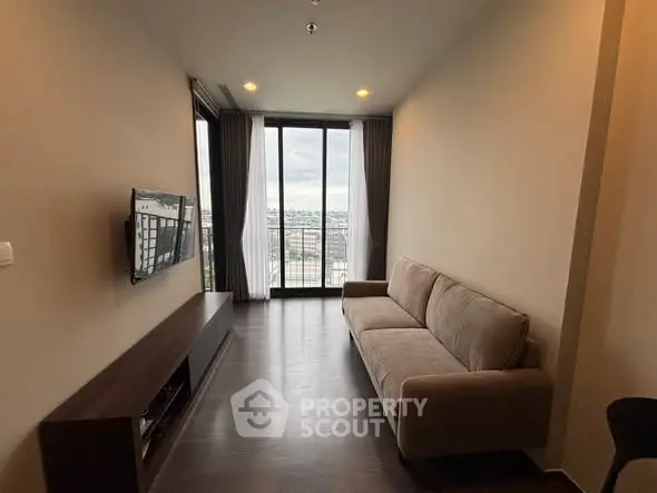 Modern living room with large windows and city view, featuring a sleek sofa and wall-mounted TV.