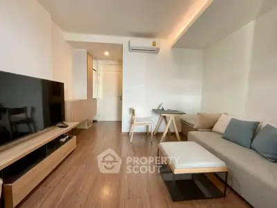Modern living room with sleek furniture and wooden flooring, featuring a large TV and cozy seating area.