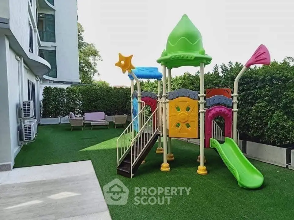 Charming outdoor playground area in modern residential complex with lush greenery and colorful play structures.