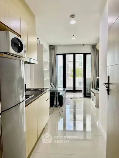 Modern apartment kitchen with sleek appliances and open layout leading to a bright living area.