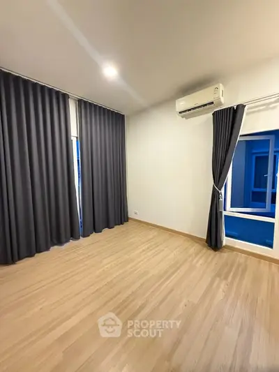 Spacious bedroom with wooden flooring and large window, featuring modern air conditioning and elegant curtains.
