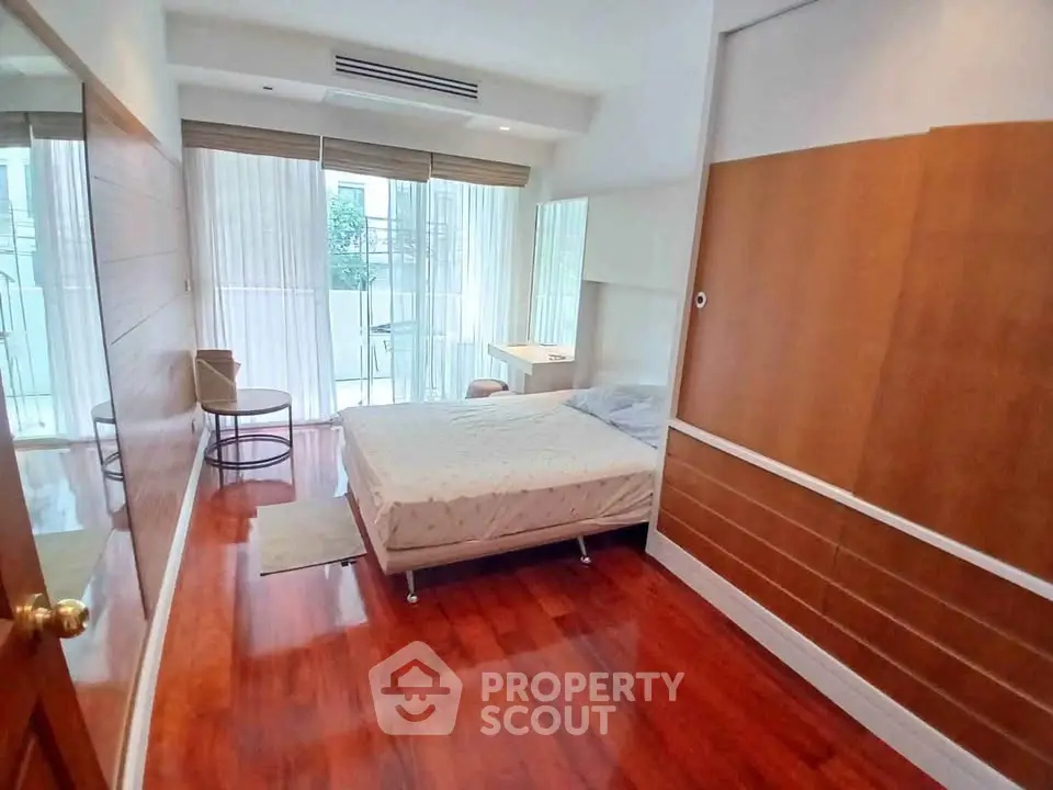 Spacious bedroom with wooden flooring and large windows in modern apartment.