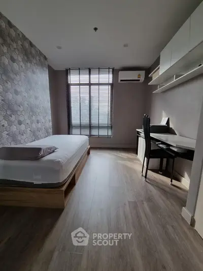 Modern bedroom with stylish decor, featuring a bed, desk, and large window for natural light.