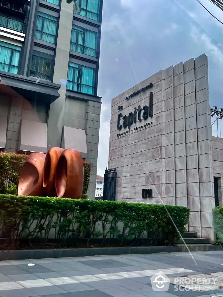 Modern building entrance with unique sculpture and lush greenery.