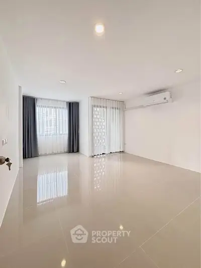 Spacious empty room with glossy tiled floors and large windows, ideal for customization.