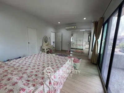 Spacious bedroom with floral bedding, large windows, and elegant decor