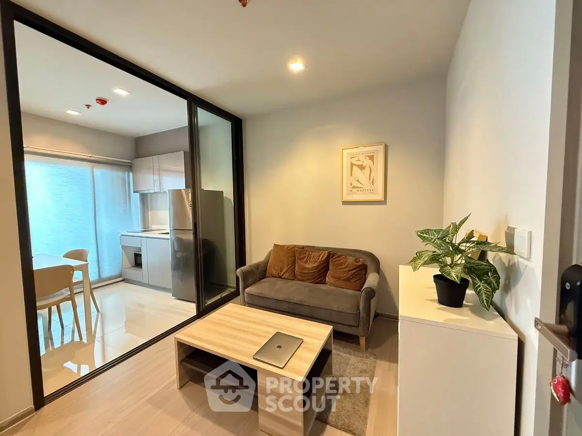 Modern living room with glass partition and cozy kitchen area, featuring stylish decor and natural light.