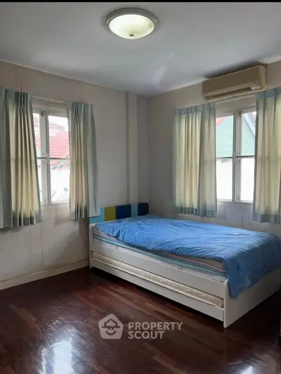 Cozy bedroom with wooden flooring and natural light, featuring a single bed and air conditioning.