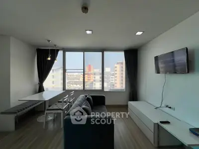 Modern living room with large windows and city view, featuring a sleek sofa and wall-mounted TV.