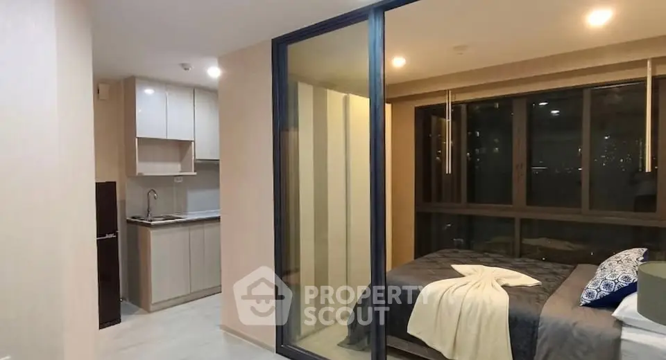 Modern studio apartment with glass partition, cozy bedroom, and compact kitchen.
