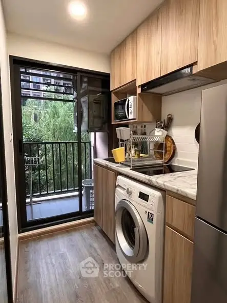 Modern kitchen with balcony view, featuring washing machine and sleek wooden cabinets.
