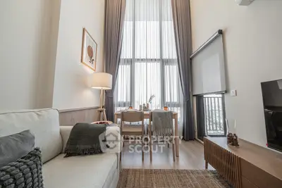 Modern living room with high ceilings and elegant decor, featuring a cozy sofa and dining area with large windows.