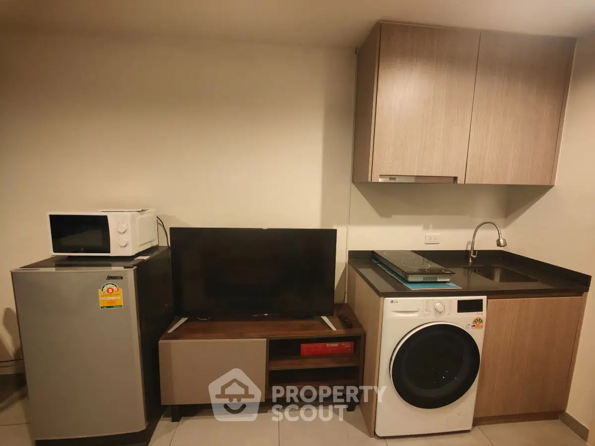 Modern compact kitchen with appliances including fridge, microwave, and washing machine in a cozy apartment.