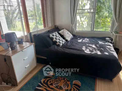 Cozy bedroom with large windows and stylish decor, featuring a tiger-themed rug and natural light.
