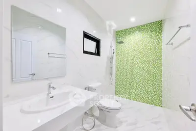 Modern bathroom with green mosaic shower wall and sleek white fixtures.