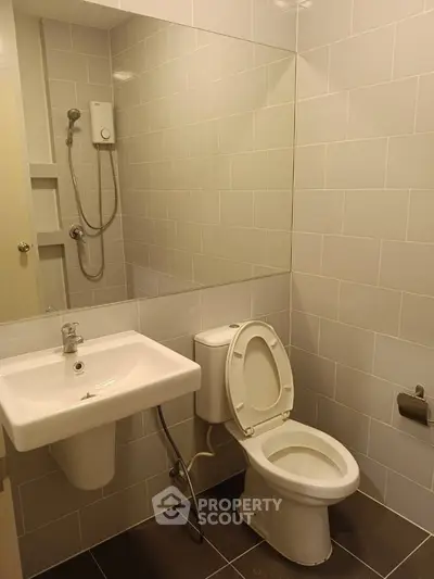 Compact and clean bathroom with wall-mounted sink, toilet, and shower, featuring neutral tile work and practical design.