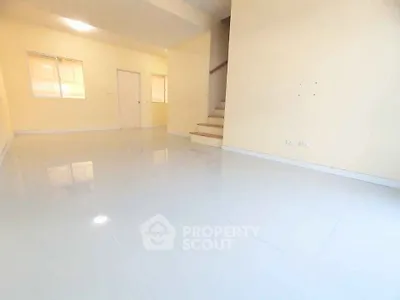 Spacious minimalist living room with glossy white flooring and staircase
